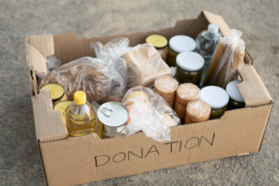 A cardboard box labeled "Donation" that is filled with nonperishables such as oil, canned food, and pasta