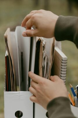 Hands sorting through papers, notebooks, and folders stored in a file organizer